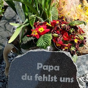 Grab mit Blumen und Gedenkstein mit der Inschrift Papa du fehlst uns geschmückt