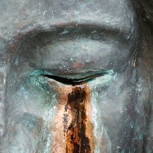 Gesicht einer Skulptur mit geschlossenen Augen und Tränen aus Rost