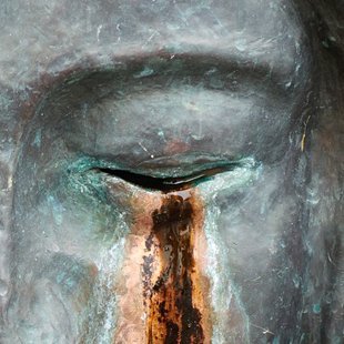 Gesicht einer Skulptur mit geschlossenen Augen und Tränen aus Rost