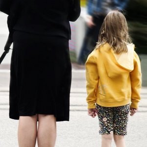 Kind mit gelber Jacke steht neben Frau in schwarzer Kleidung