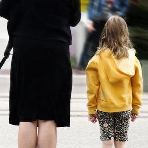 Kind mit gelber Jacke steht neben Frau in schwarzer Kleidung