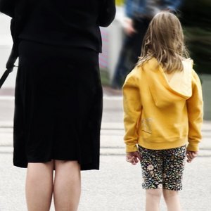 Kind mit gelber Jacke steht neben Frau in schwarzer Kleidung