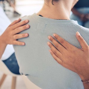 Zwei Personen legen einer Frau ihre Hände auf den Rücken