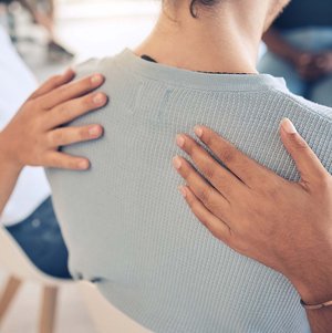 Zwei Personen legen einer Frau ihre Hände auf den Rücken
