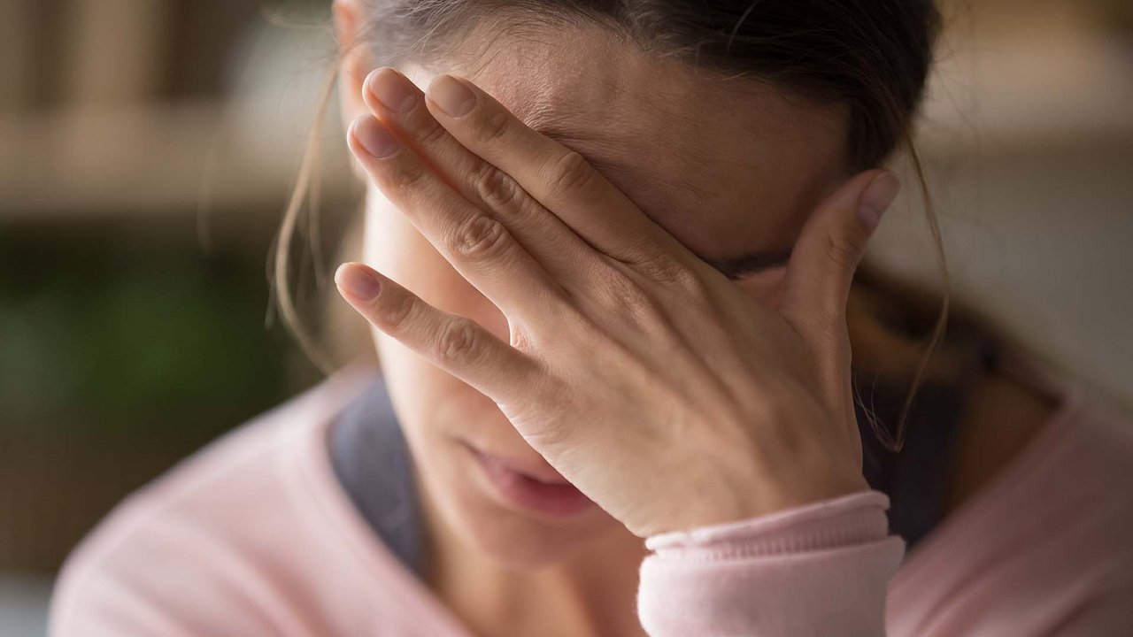 Frau fasst sich an die Stirn und bedeckt ihre Augen