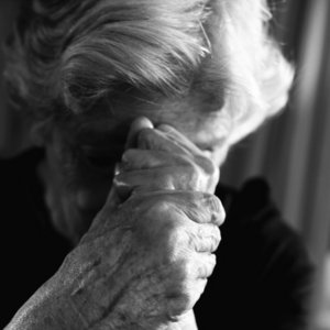 Ältere Frau senkt den Kopf in ihre ineinanderfassenden Hände