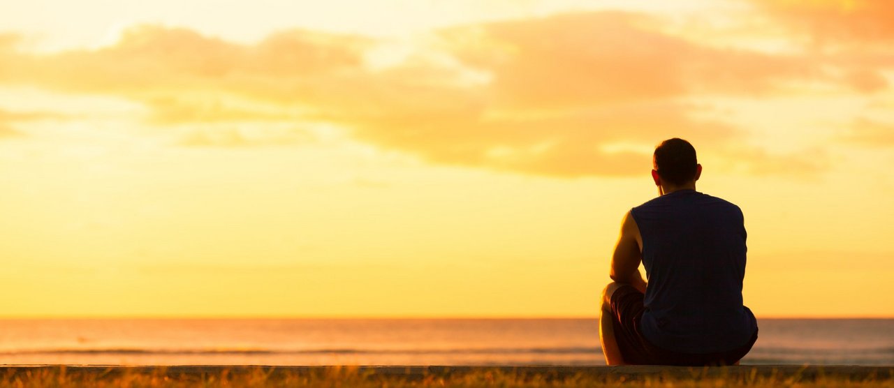 Mann sitzt allein im Sonnenuntergang am Meer