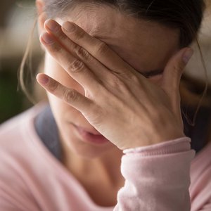 Frau verdeckt ihre Augen und ihre Stirn mit ihrer Hand