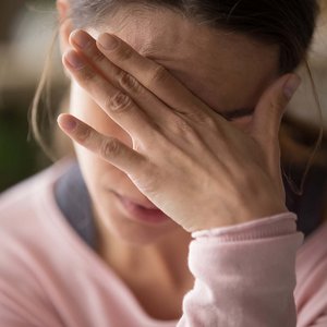 Frau verdeckt ihre Augen und ihre Stirn mit ihrer Hand