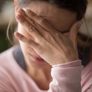 Frau verdeckt ihre Augen und ihre Stirn mit ihrer Hand