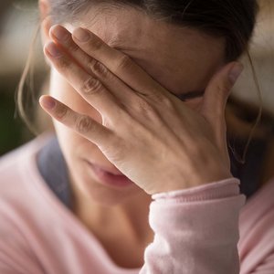 Frau verdeckt ihre Augen und ihre Stirn mit ihrer Hand