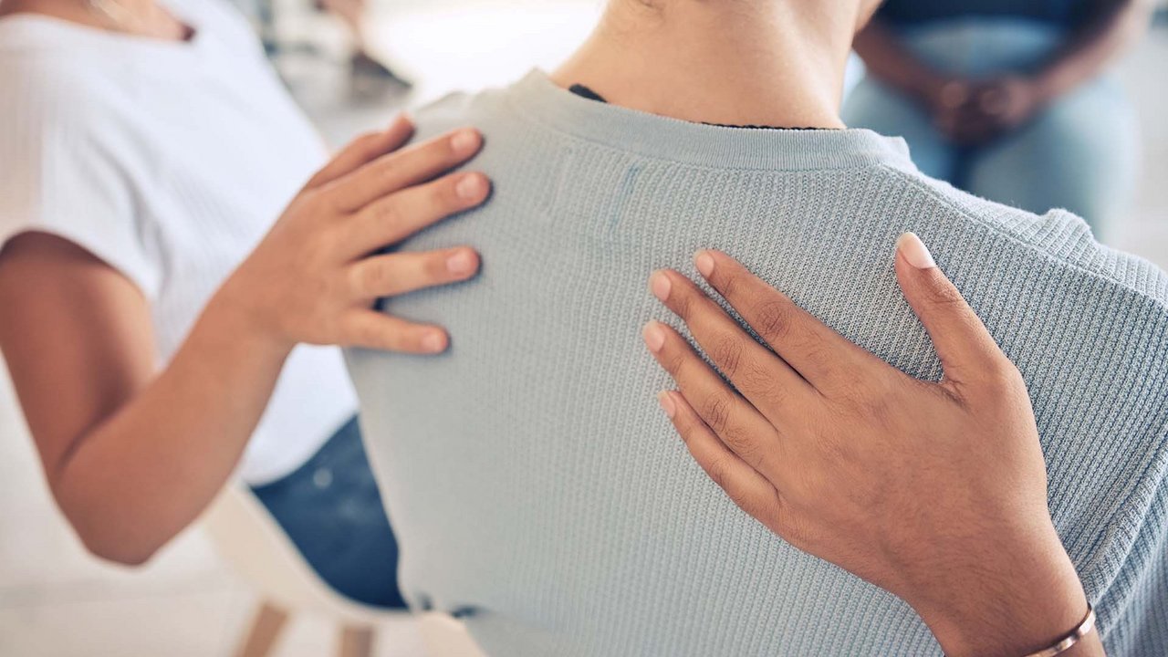 Zwei Menschen legen einer Frau die Hand auf den Rücken