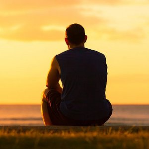 Mann sitzt allein im Sonnenuntergang am Meer