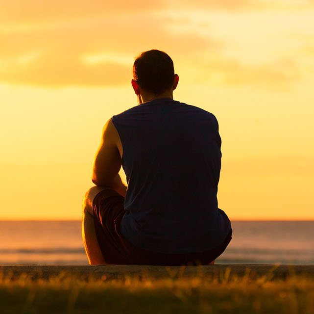 Mann sitzt allein im Sonnenuntergang am Meer
