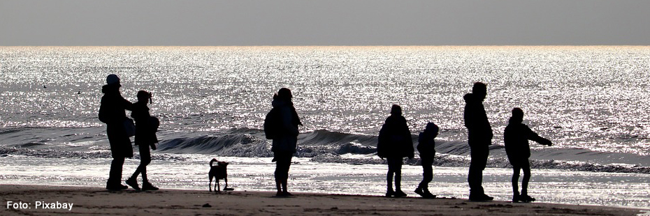 Menschen verschiedenen Alters am Strand im Gegenlicht